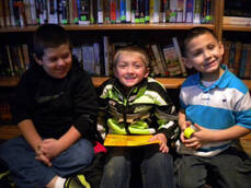 3 smiling young boys reading together in the library